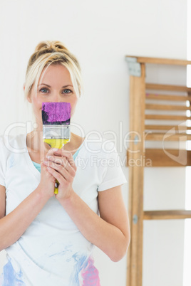Woman holding paint brush in front of face at new house