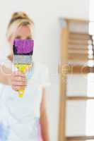 Blurred woman holding out paint brush at new house