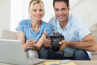 Happy couple with camera and laptop on sofa in living room