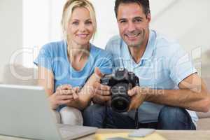 Happy couple with camera and laptop on sofa in living room