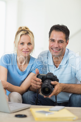 Happy couple with camera and laptop on sofa in living room