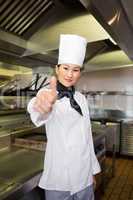 Smiling female cook gesturing thumbs up in kitchen