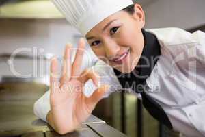 Smiling female cook gesturing okay sign in kitchen