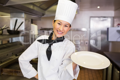 Smiling female cook holding empty plate in kitchen