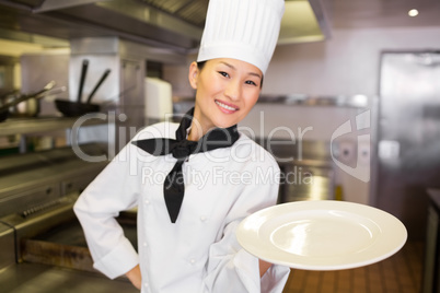 Smiling female cook holding empty plate in kitchen