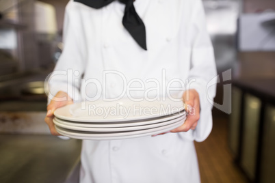 Mid section of a female cook holding empty plates in kitchen