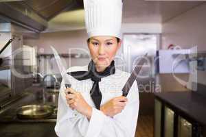 Confident female cook holding knives in kitchen