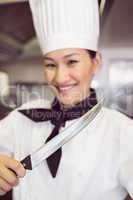 Smiling female cook holding knife in kitchen