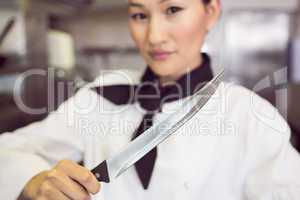 Confident female cook holding knife in kitchen