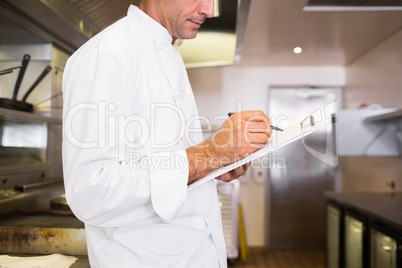 Concentrated male cook writing on clipboard in kitchen