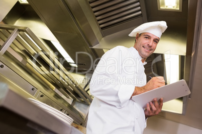 Smiling male cook writing on clipboard in kitchen