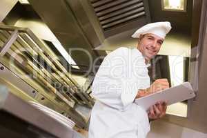 Smiling male cook writing on clipboard in kitchen