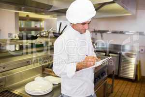 Concentrated male cook writing on clipboard in kitchen
