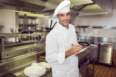 Smiling male cook writing on clipboard in kitchen