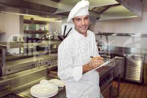 Smiling male cook writing on clipboard in kitchen