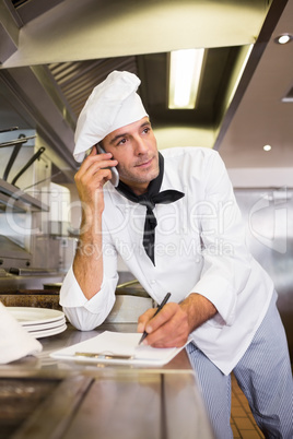 Cook writing on clipboard while using cellphone in kitchen
