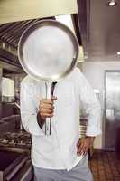 Cook holding pan in front of face in kitchen