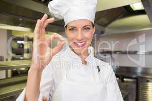 Smiling female cook gesturing okay sign in kitchen