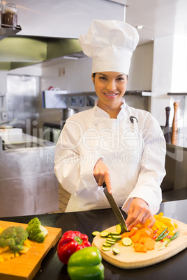 Smiling female chef cutting vegetables in kitchen