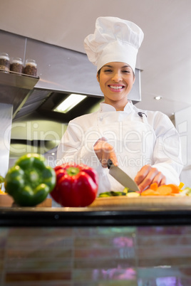 Smiling female chef cutting vegetables in kitchen