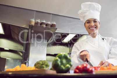 Smiling female chef cutting vegetables in kitchen