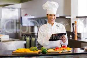 Smiling chef using digital tablet while cutting vegetables
