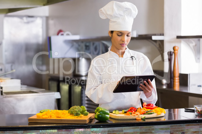 Female chef using digital tablet while cutting vegetables