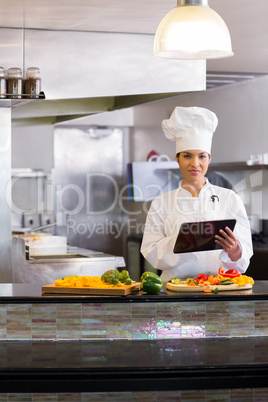 Female chef using digital tablet while cutting vegetables in kit