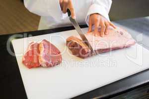 Mid section of hands cutting meat in kitchen