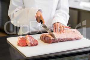 Mid section of hands cutting meat in kitchen