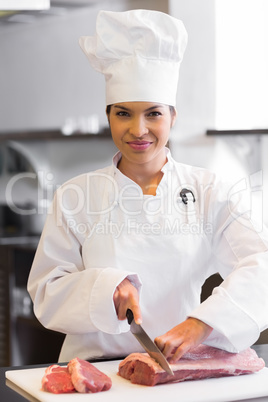 Smiling female chef cutting meat in kitchen