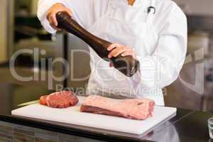 Mid section of female chef grinding pepper over meat