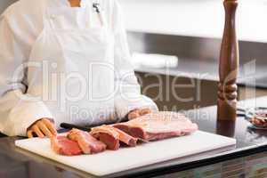 Mid section of chef with cut meat pieces in kitchen