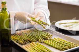 Hands with fresh asparagus and oil in kitchen