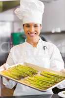 Smiling chef holding tray of fresh asparagus in kitchen