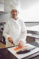 Smiling male chef cutting fish in kitchen