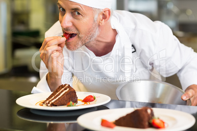 Smiling male pastry chef eating strawberry by dessert