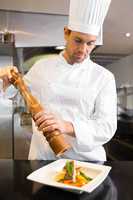 Concentrated male cook grinding pepper on food in kitchen