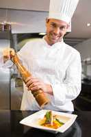 Smiling male cook grinding pepper on food in kitchen