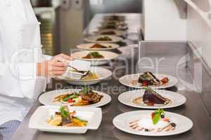 Mid section of a female chef garnishing food in kitchen