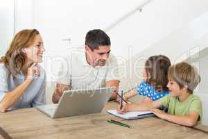 Parents with laptop assisting children coloring
