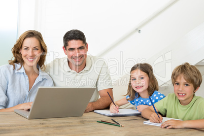 Parents with laptop while children coloring at table