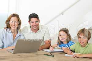 Parents with laptop while children coloring at table