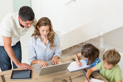 Parents using laptop while children coloring at home