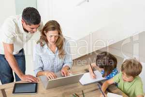 Parents using laptop while children coloring at home