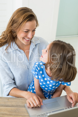 Girl looking at mother using laptop