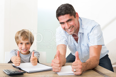 Father and son gesturing thumbs up while doing homework Father and son gesturing thumbs up while doing homework