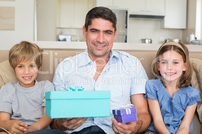 Father holding gifts by children on sofa