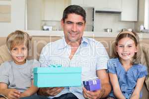 Father holding gifts by children on sofa