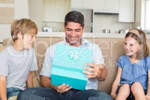 Father opening gift given by children on sofa